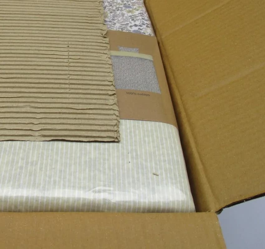 Folded striped cotton seated in a kraft export carton beside a corrugated protective insert.