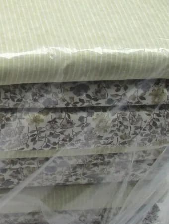 A wrapped stack of folded striped and floral cotton under clear film.