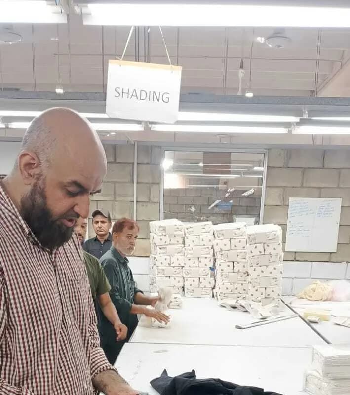 Humayun at a table marked for shade checking, with stacked finished goods behind him.